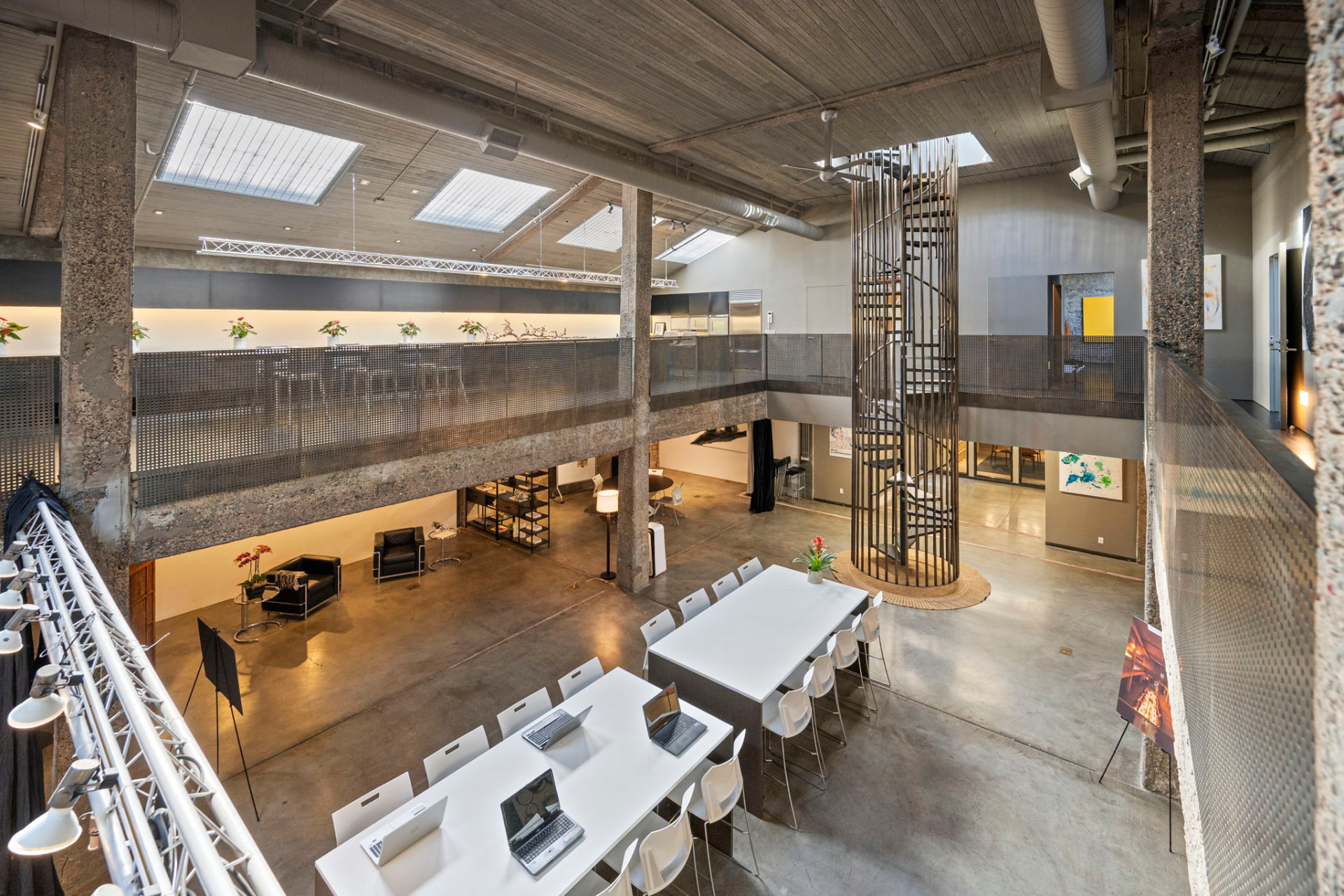 Wide interior view of the loft showing skylights, lighting truss, spiral staircase and long tables set for a working session