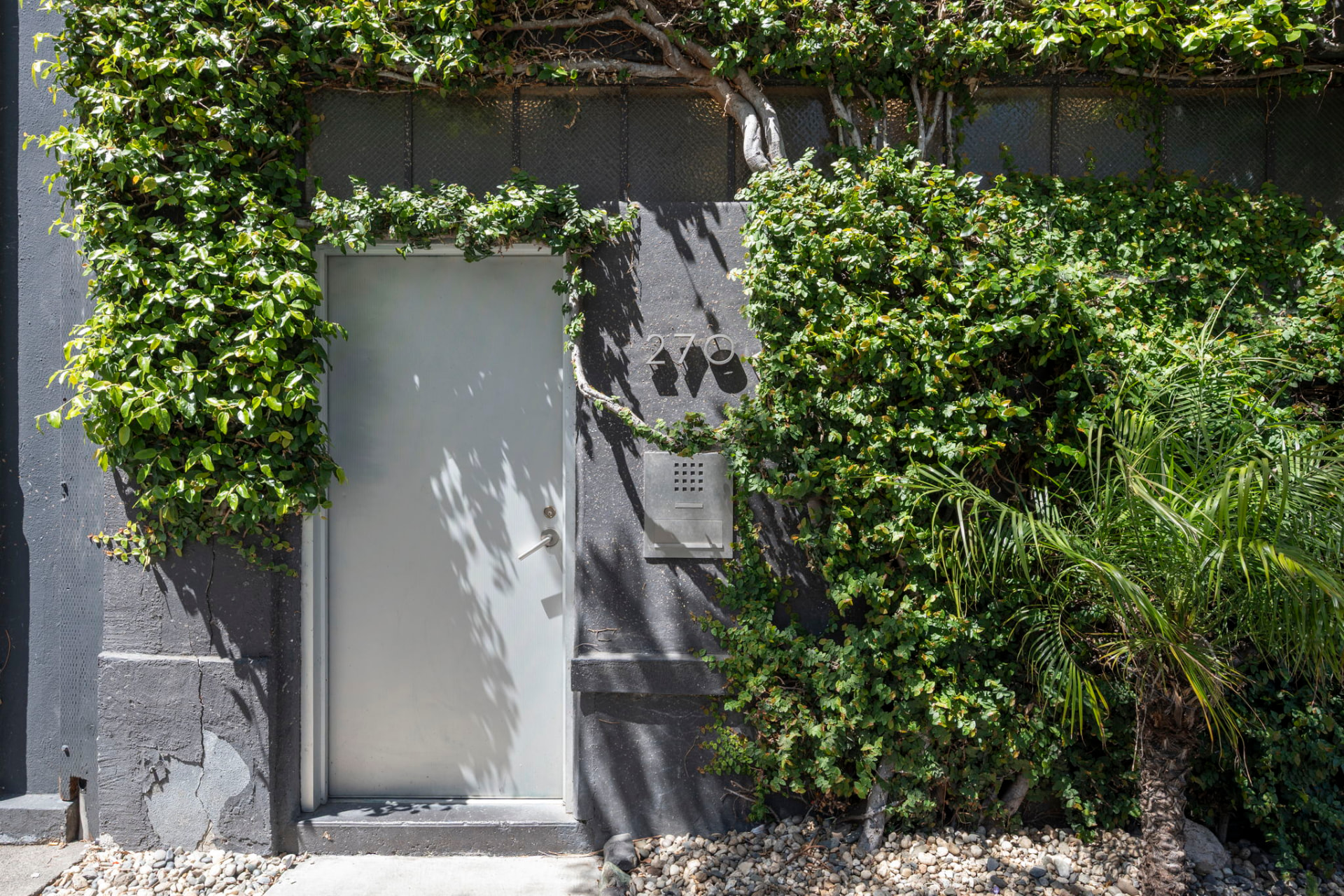 Ivy-covered concrete facade at 270 with a frosted glass entry door and intercom