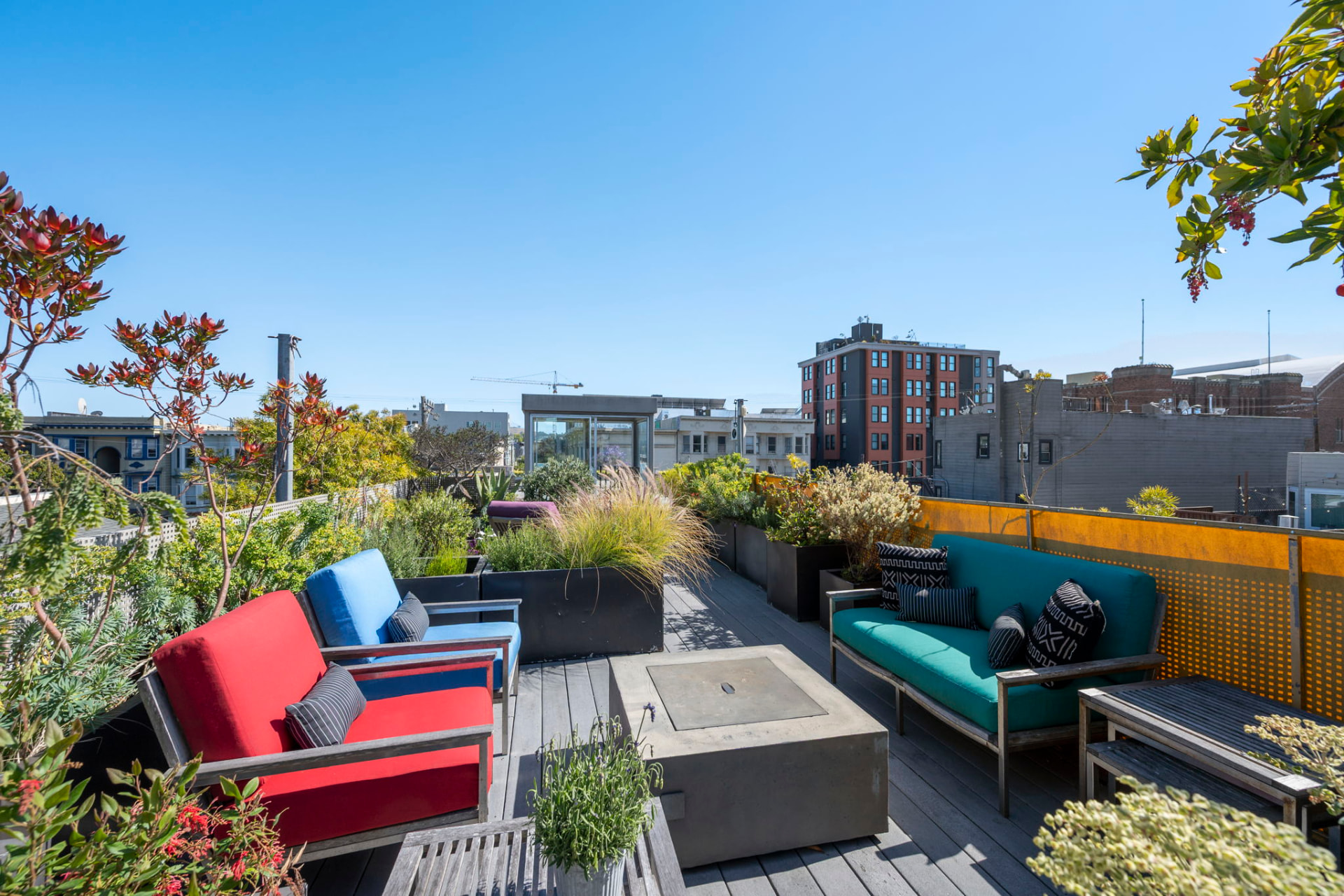 Planted roof deck with a concrete fire table, teak lounge seating and views across Mission District rooftops