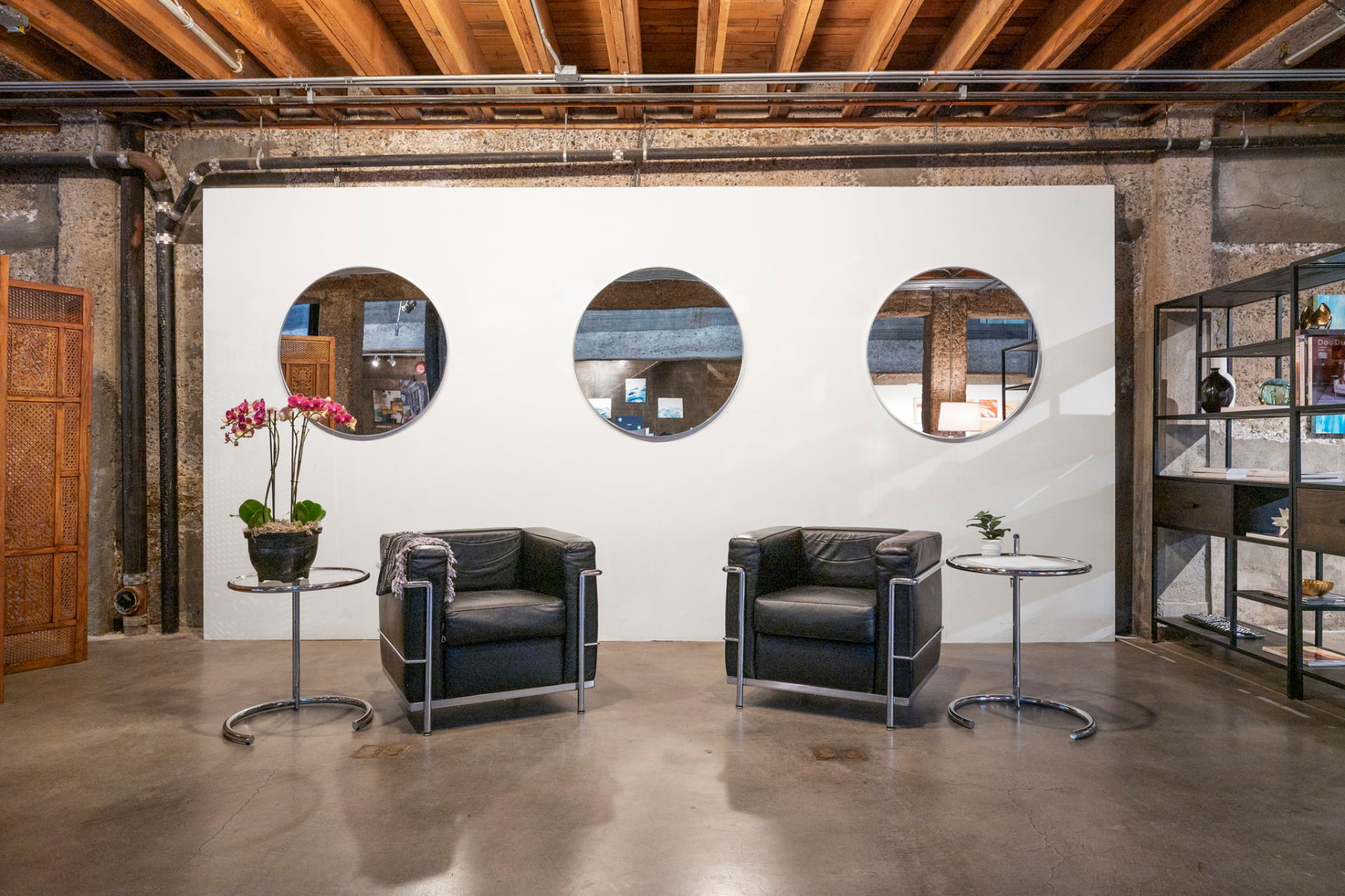 White gallery wall with three circular mirrors, two black leather armchairs and exposed timber joists above