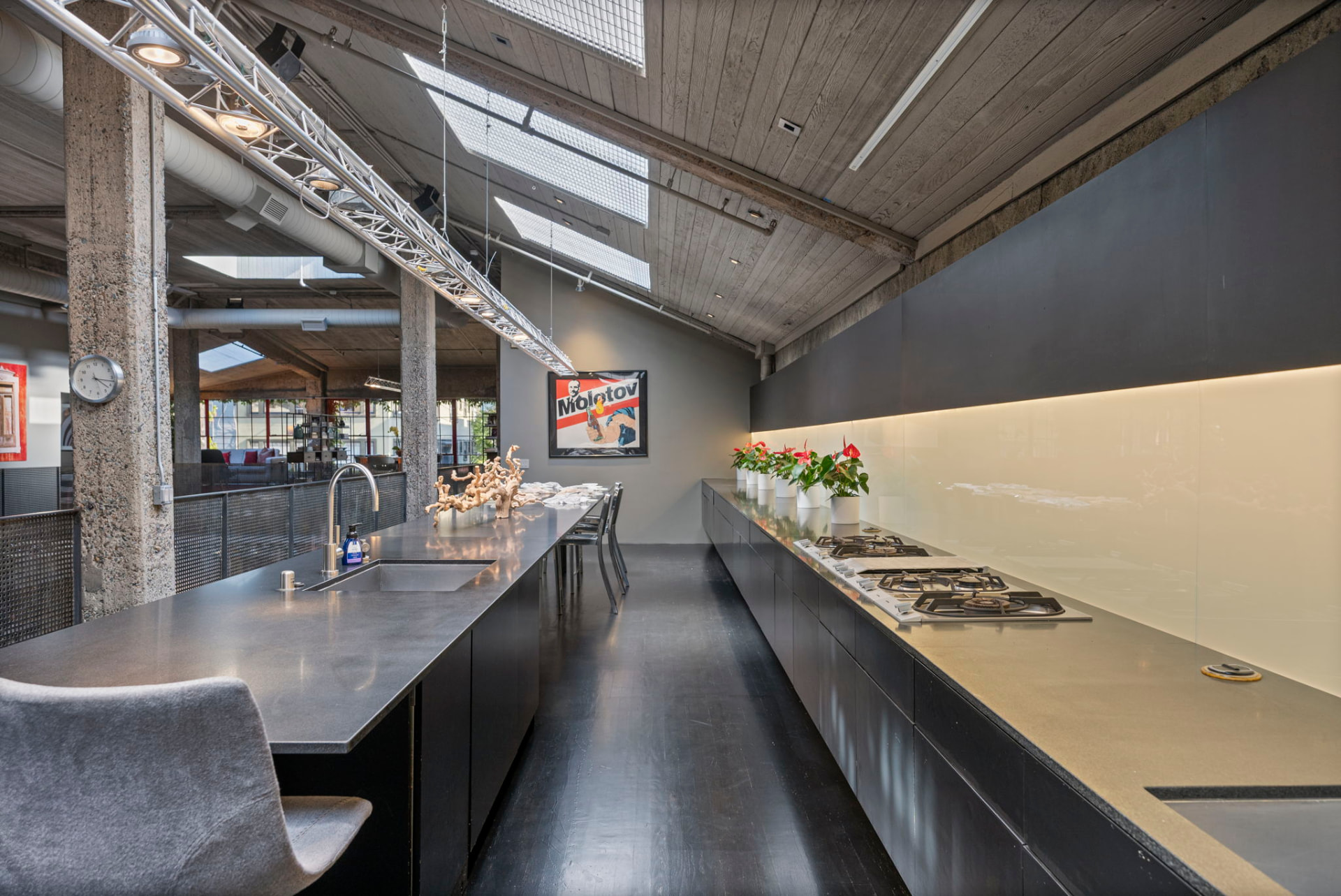 Long stone kitchen island and gas range under angled skylights, with counter seating along one side