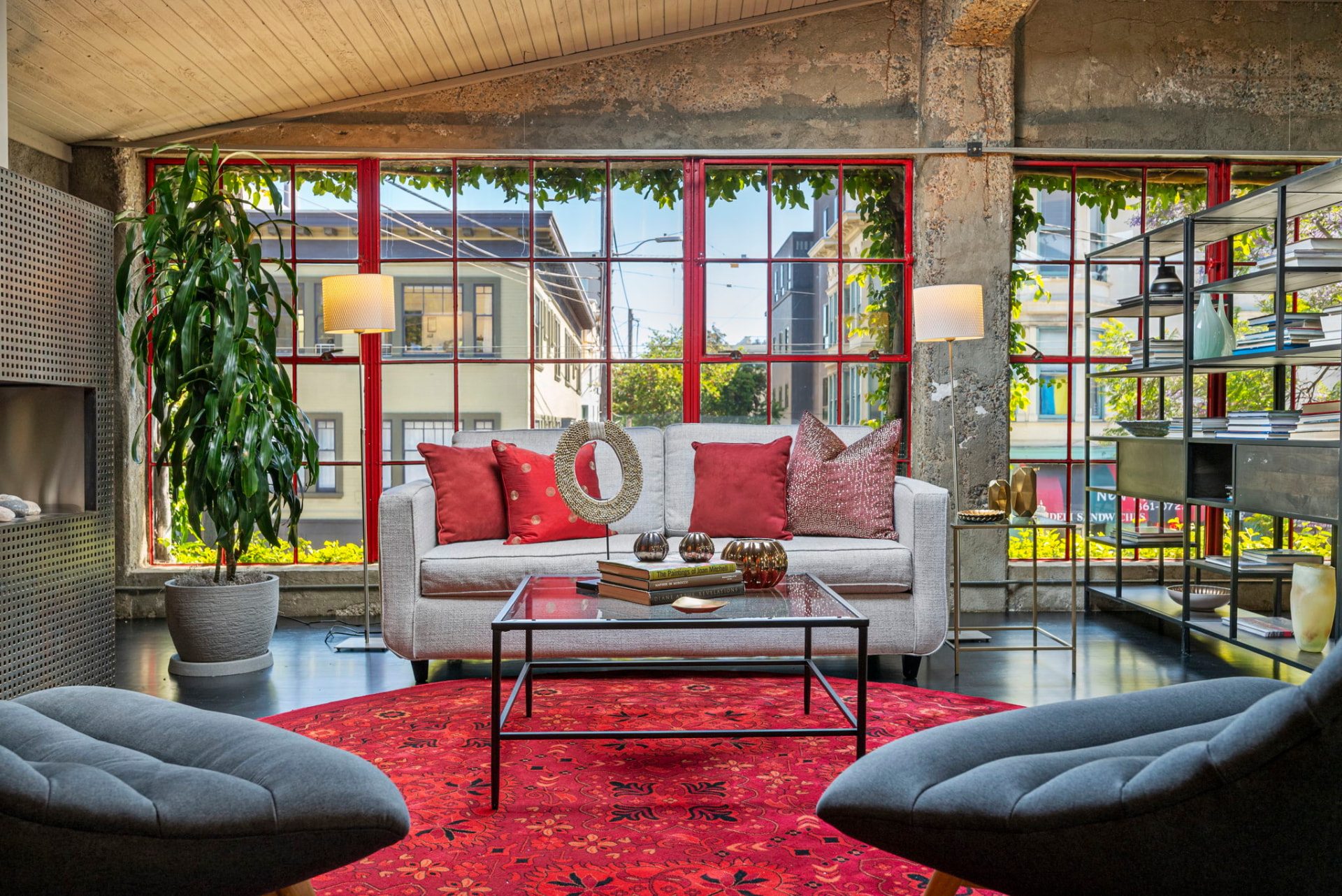 Front mezzanine lounge with a sofa framed by tall red steel factory windows overlooking the Mission District street