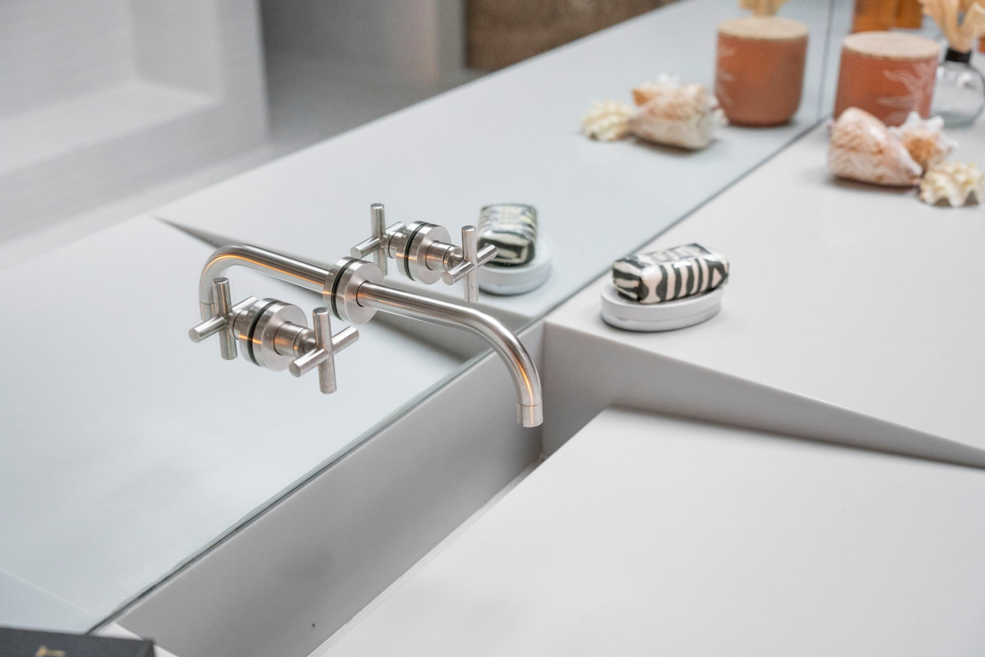 Wall-mounted brushed steel fixtures over a minimal white stone basin