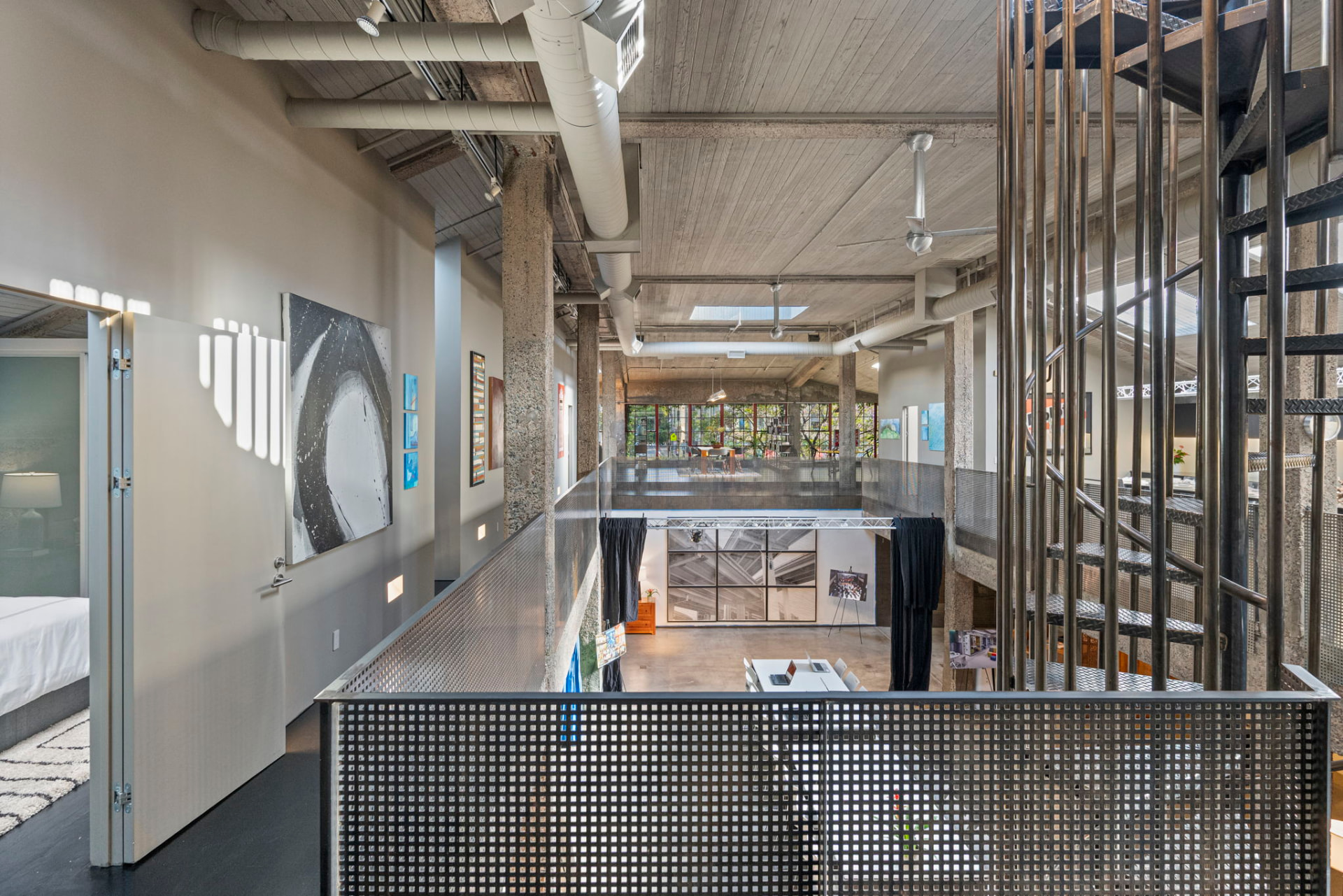 Mezzanine walkway with artwork on the wall, a spiral steel staircase and daylight falling across the floor